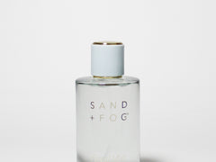 Hair perfume bottle, clear glass with gold cap and “SAND + FOG” label, 107 ml