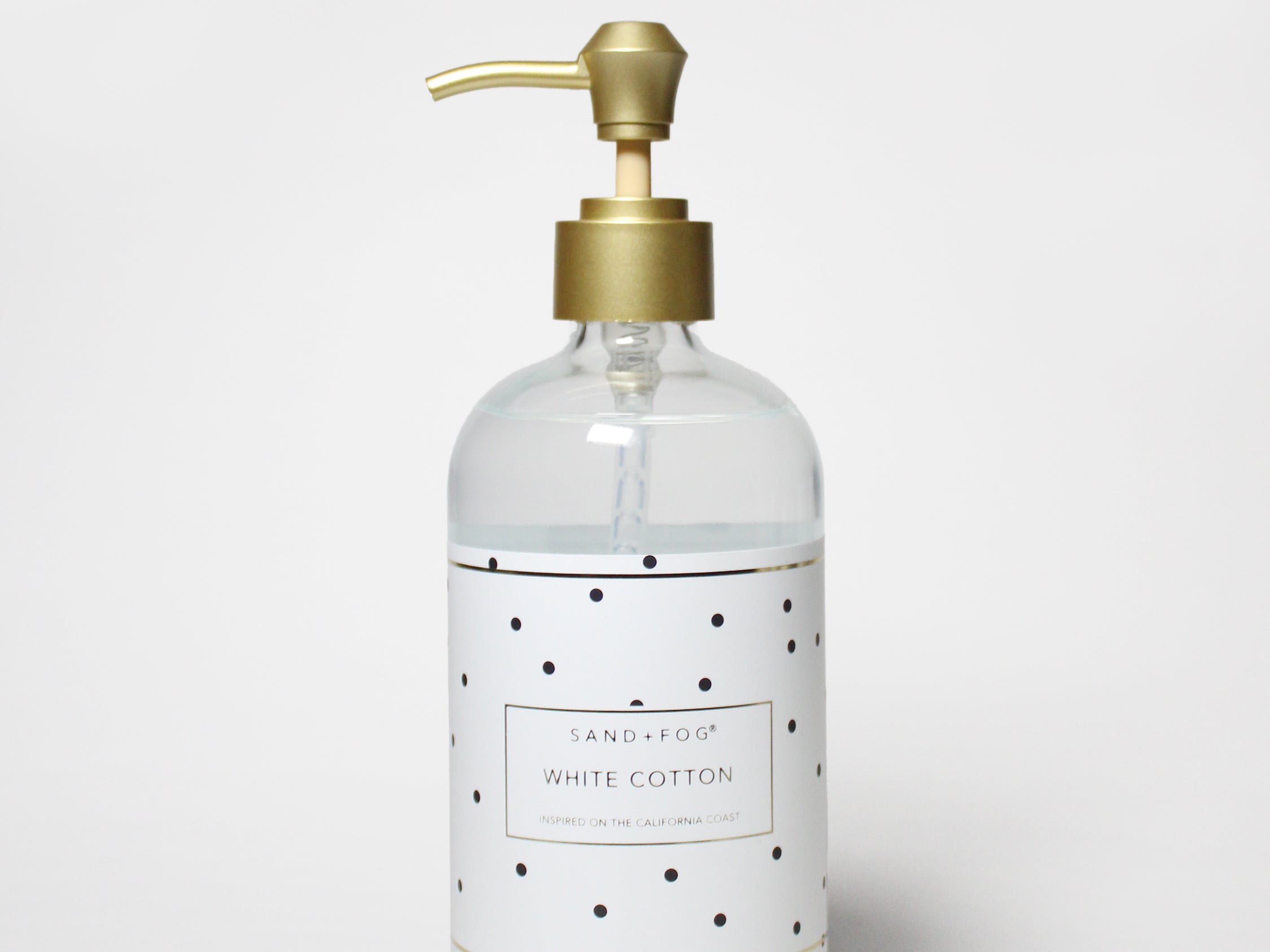 Clear liquid hand soap bottle with gold pump, white label with black dots