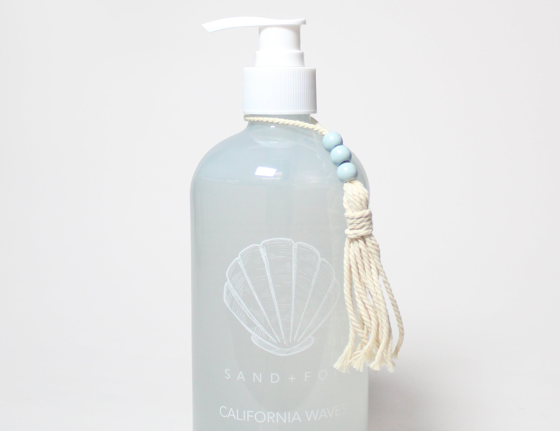 Blue-tinted liquid hand soap bottle with white pump, seashell label and tassel