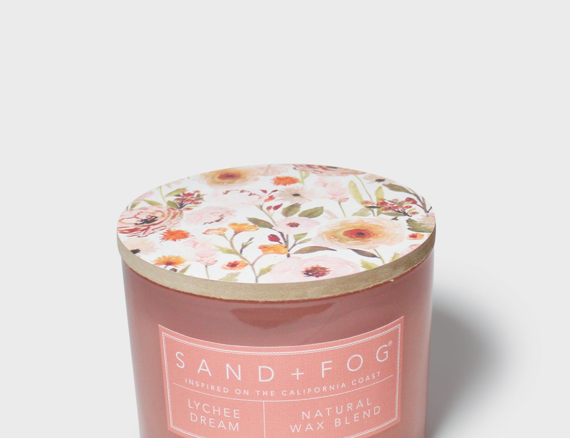 Scented candle in pink glass jar with floral lid and Sand+Fog label