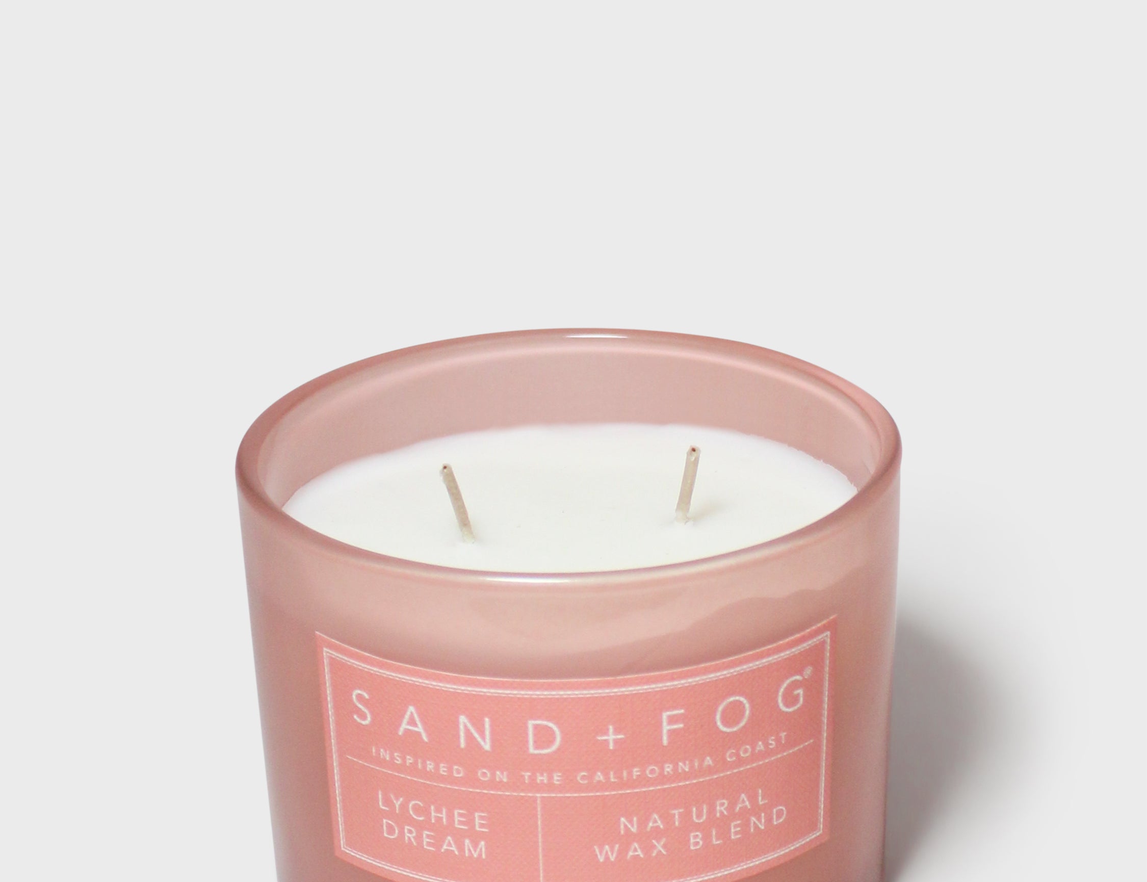 Scented candle in pink glass jar with two wicks and Sand+Fog label