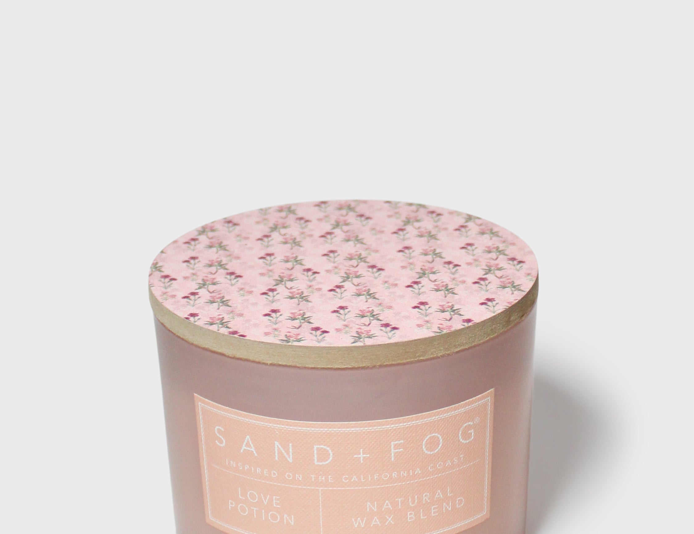 Scented candle with pink floral lid and Sand+Fog label on mauve glass jar