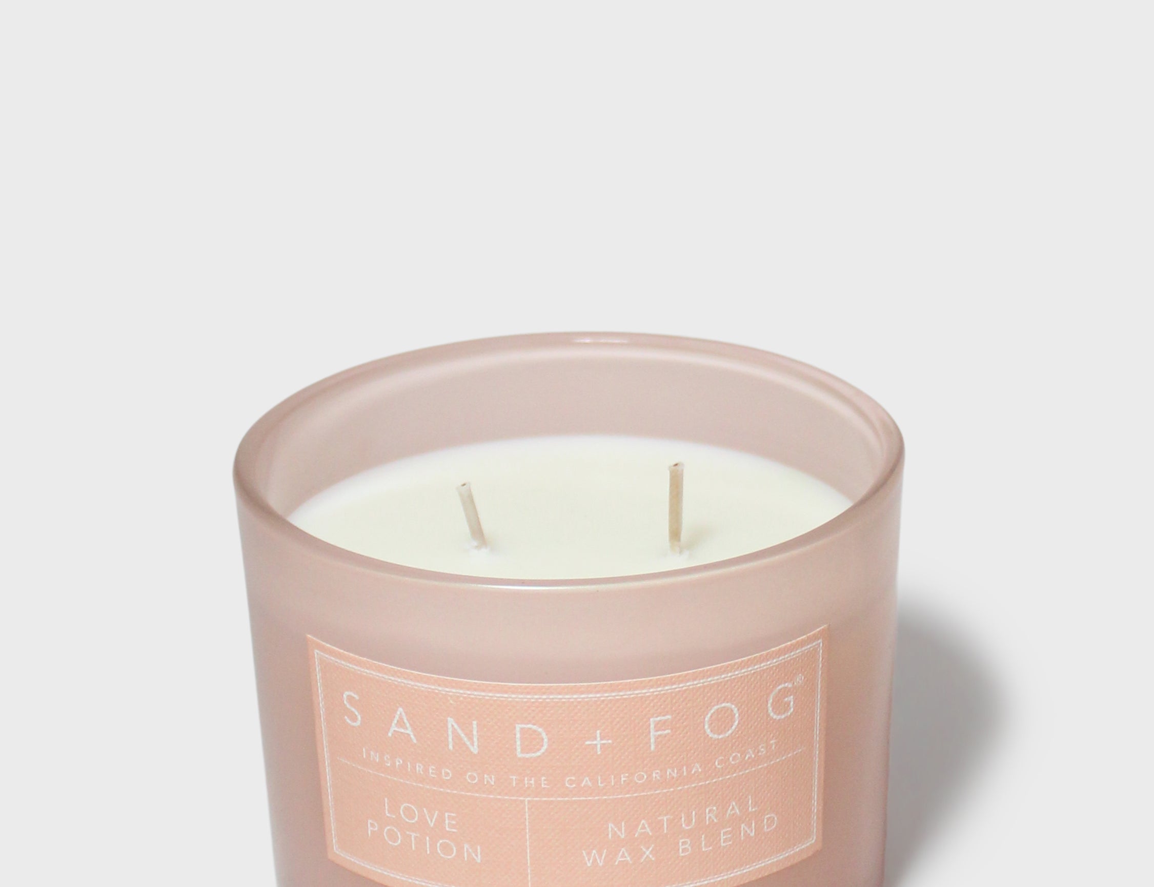 Scented candle with two wicks in cream wax, Sand+Fog label on mauve jar