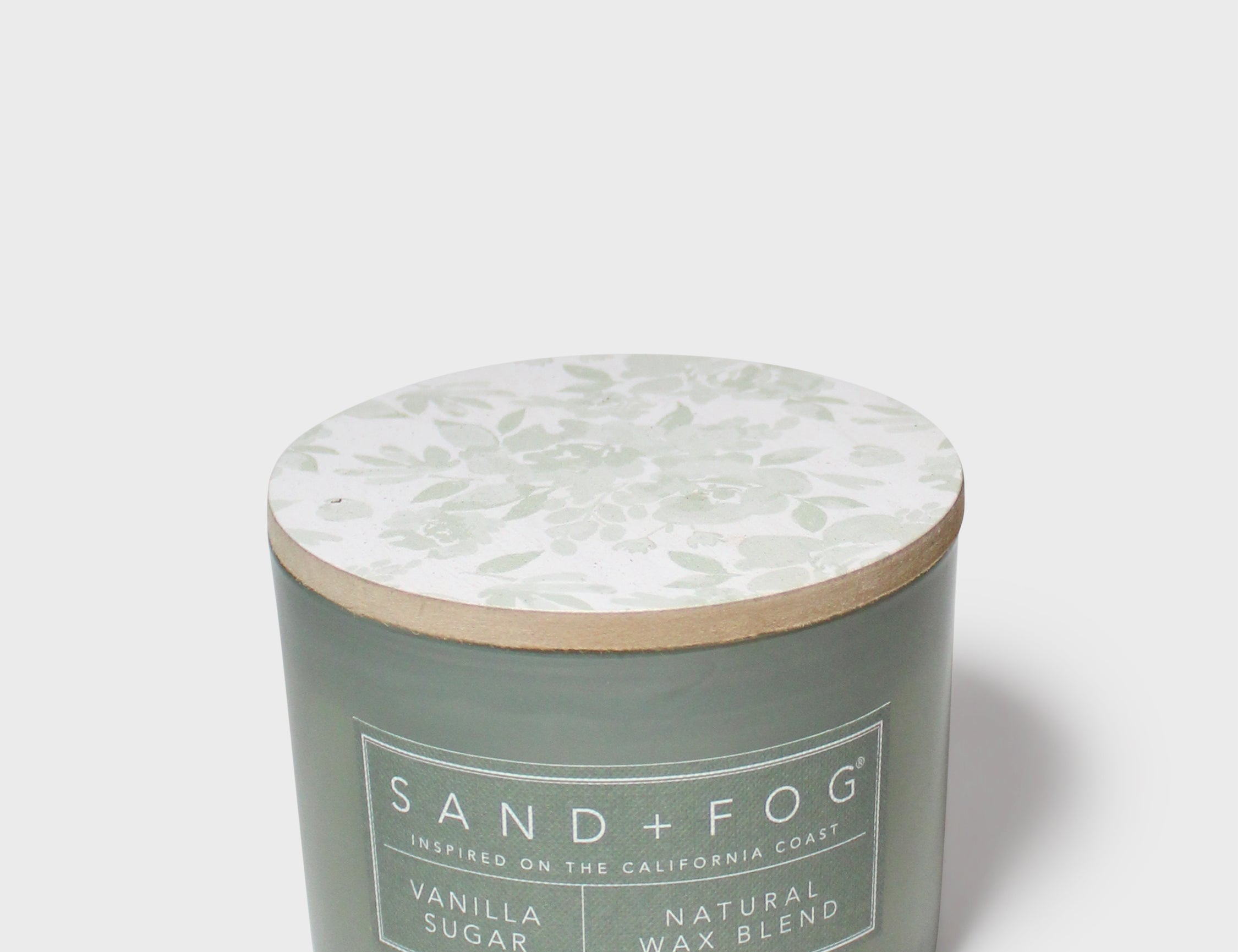 Green scented candle jar with Sand + Fog label and light wood lid, vanilla sugar