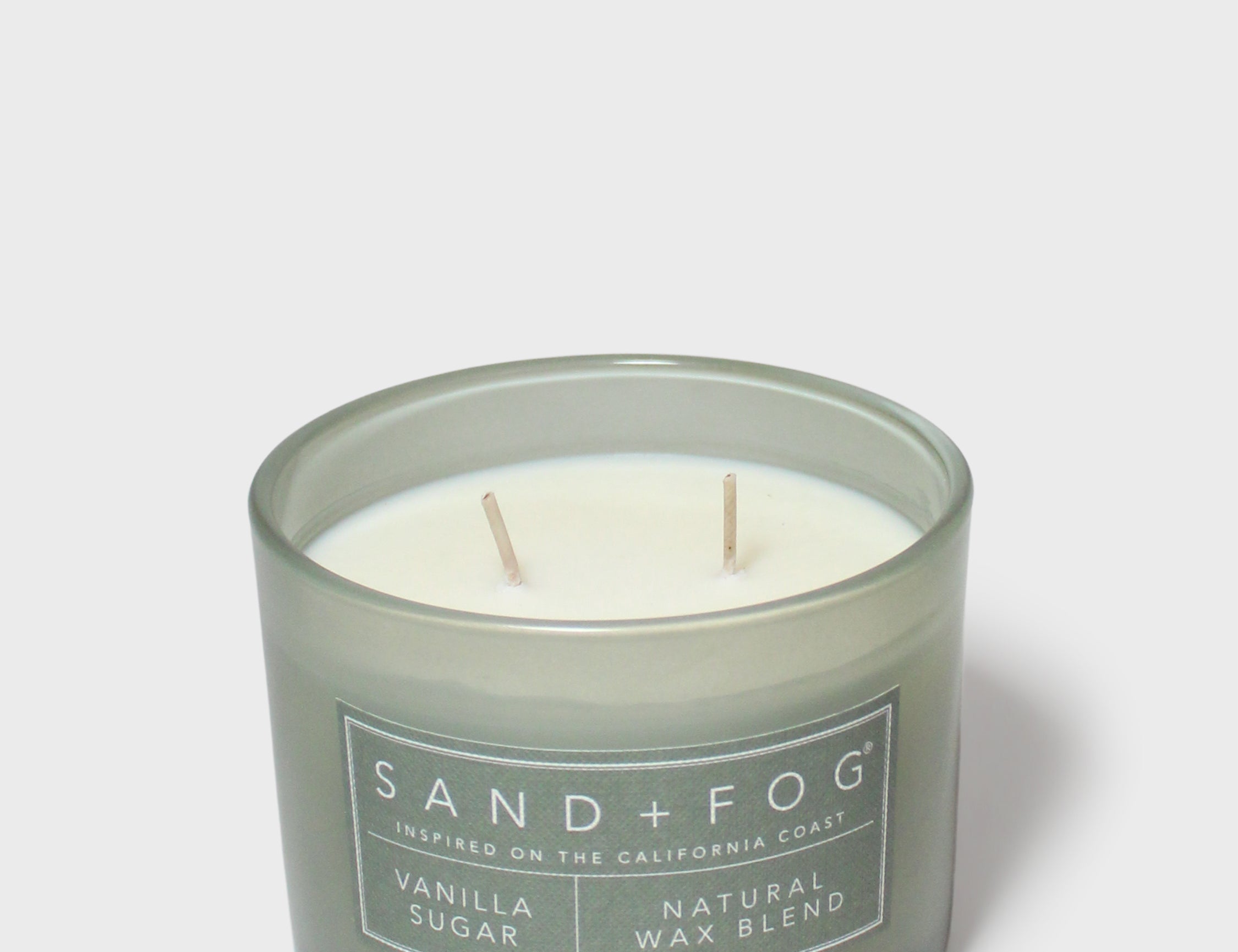 Green scented candle jar with Sand + Fog label, two wicks, vanilla sugar wax