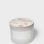White scented candle with floral lid and Sand + Fog label