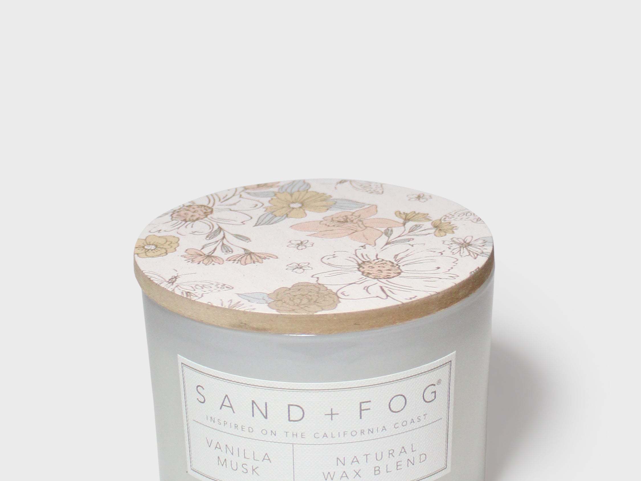 White scented candle with floral lid and Sand + Fog label