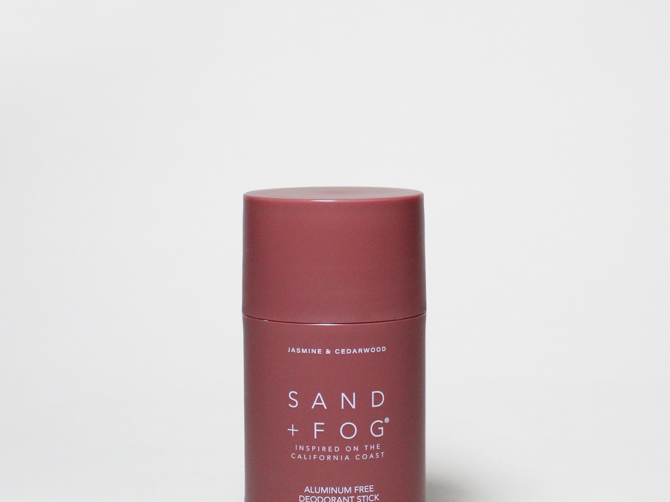 Burgundy deodorant stick with flat red cap, Sand + Fog label, 2.89 oz