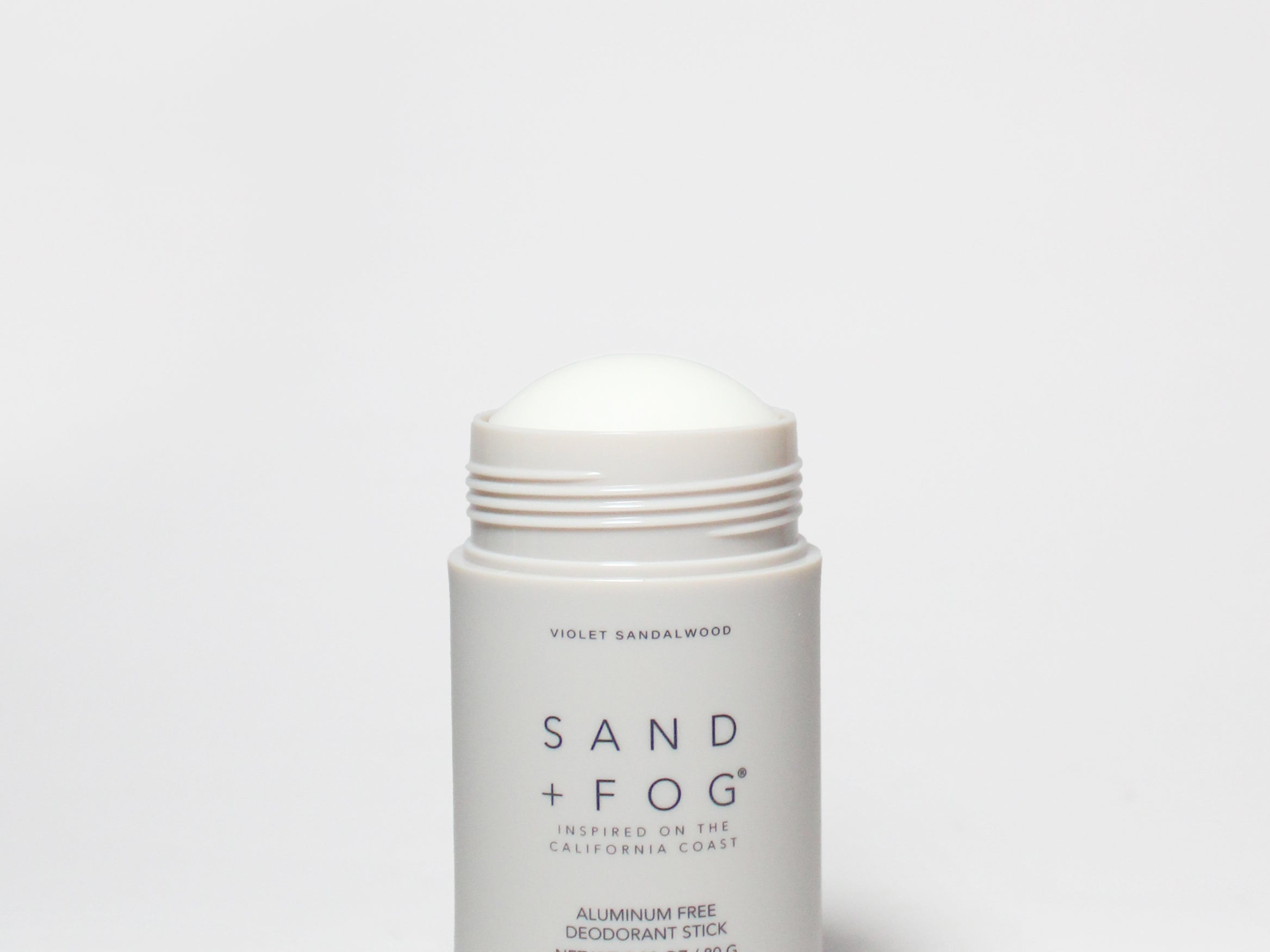SAND + FOG deodorant stick, white container with open cap and violet sandalwood label