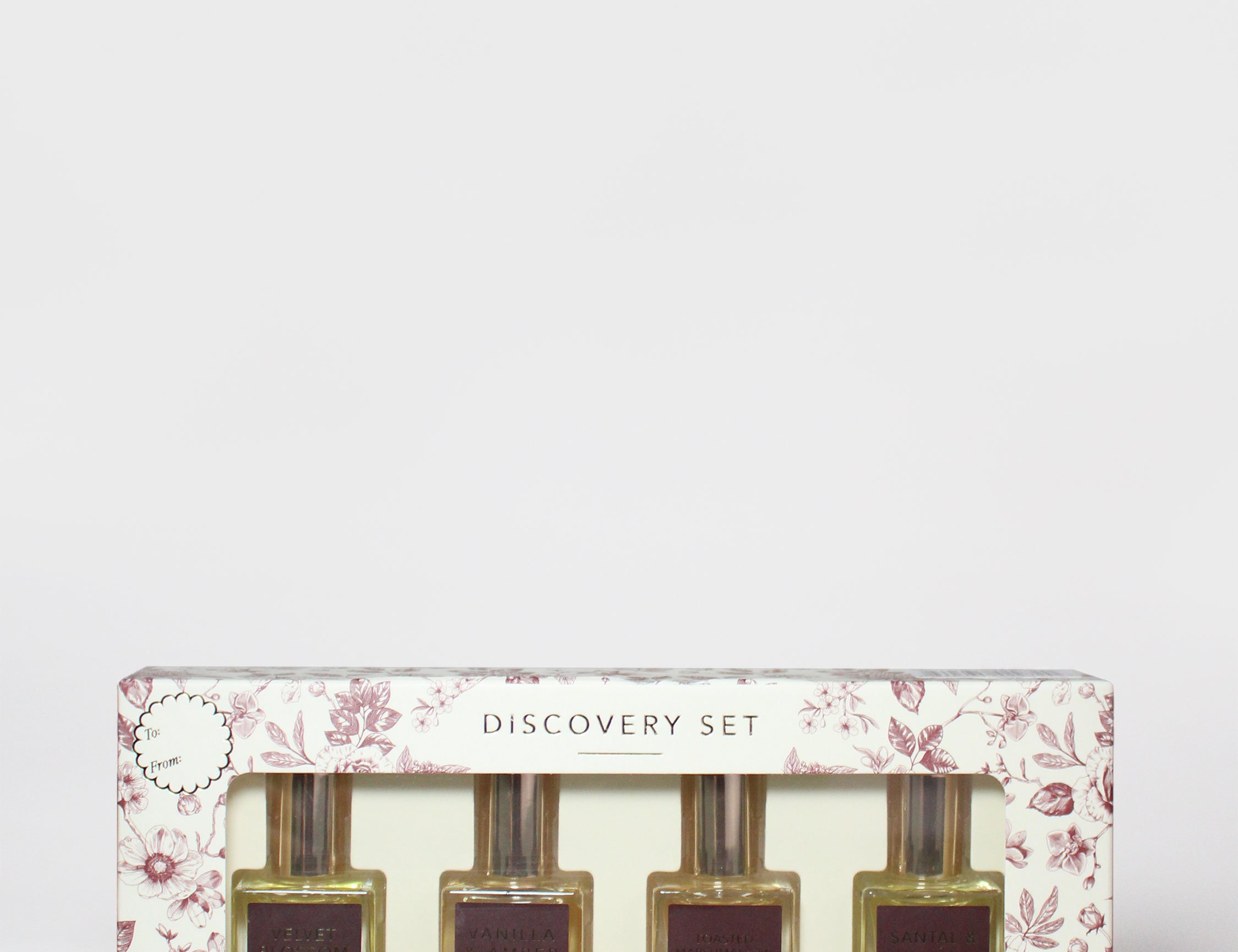 Floral perfume oil rollerball set box with four maroon-toned bottles, Sand+Fog