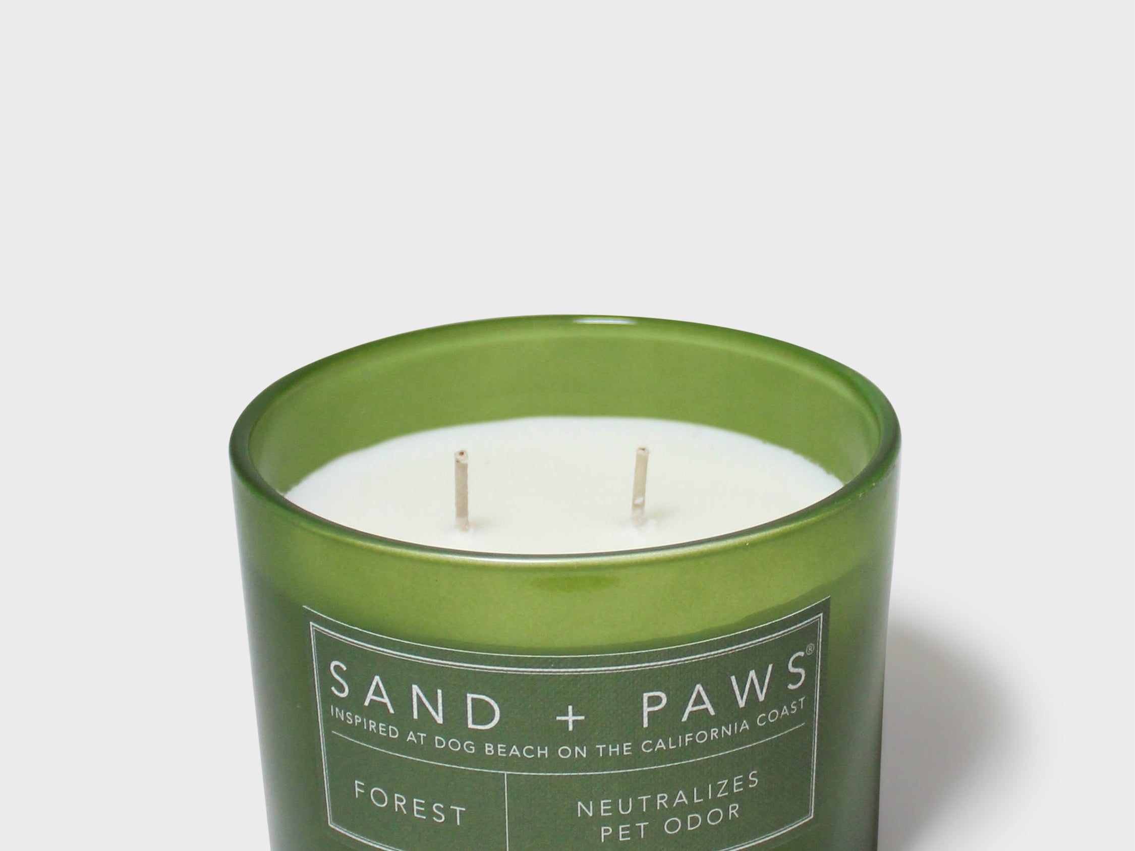 Green glass jar scented candle with white wax and Sand + Paws Forest label