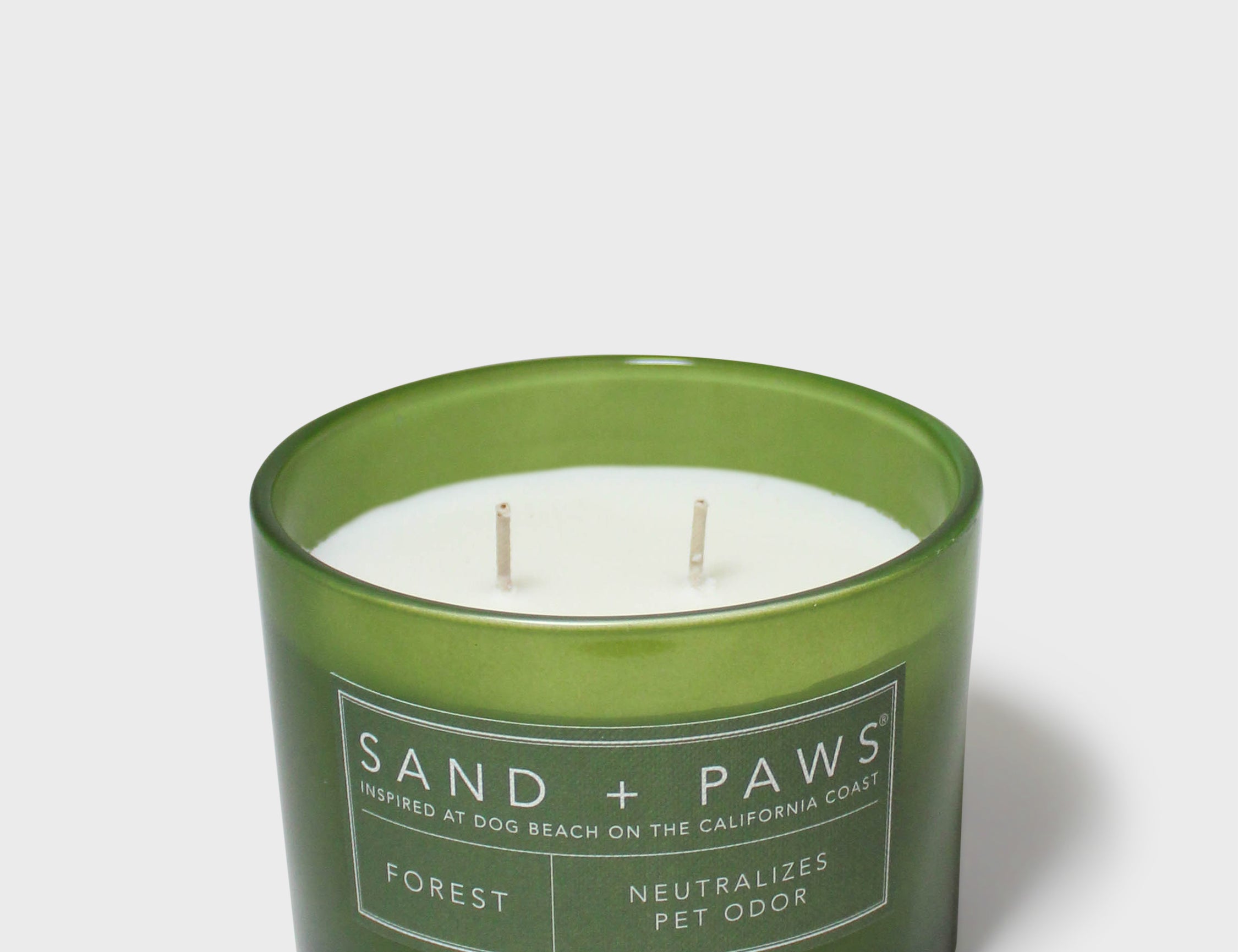 Green glass jar scented candle with white wax and Sand + Paws Forest label