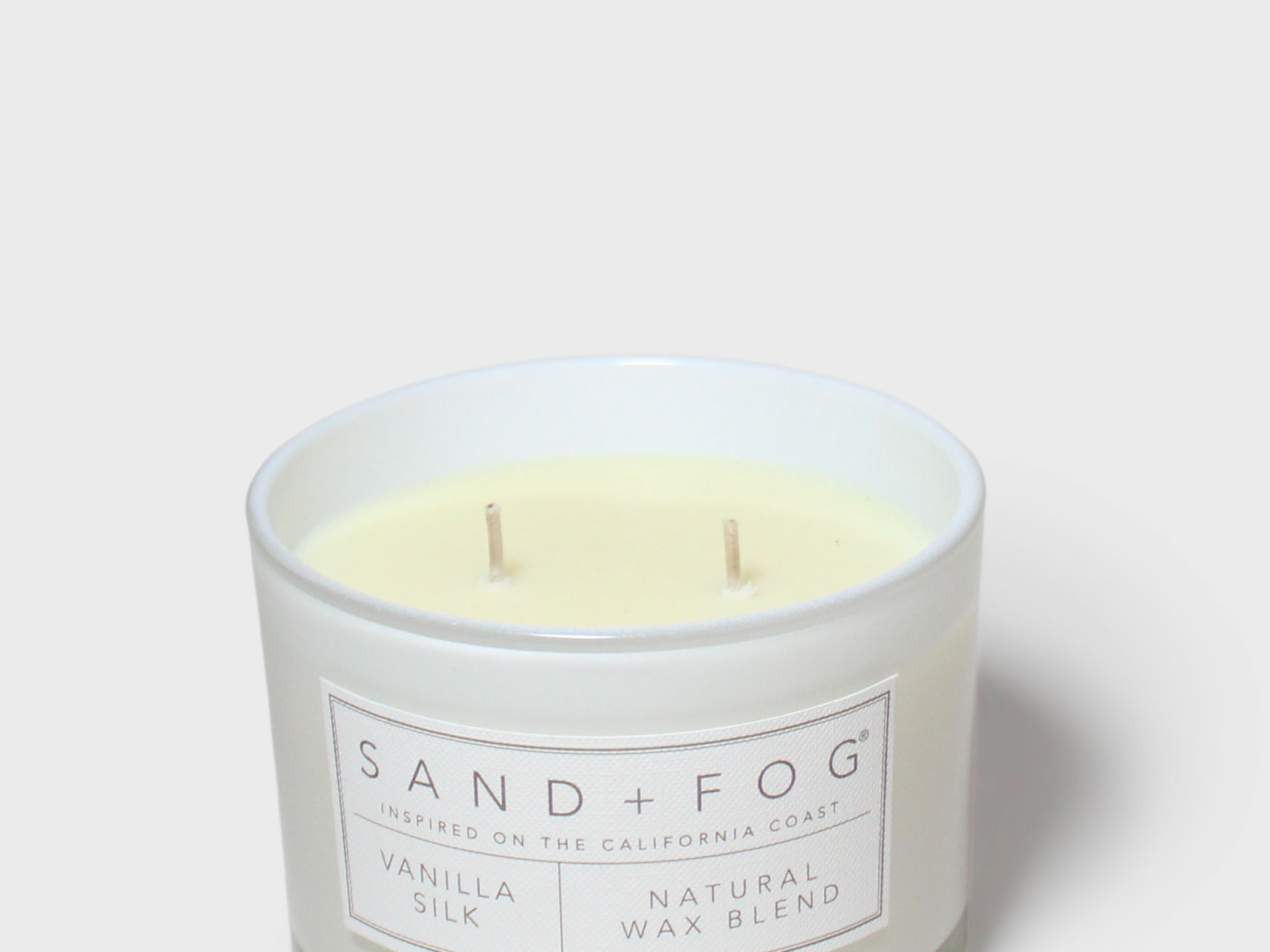 Vanilla-scented candle in frosted glass with cream wax and 'SAND+FOG' label