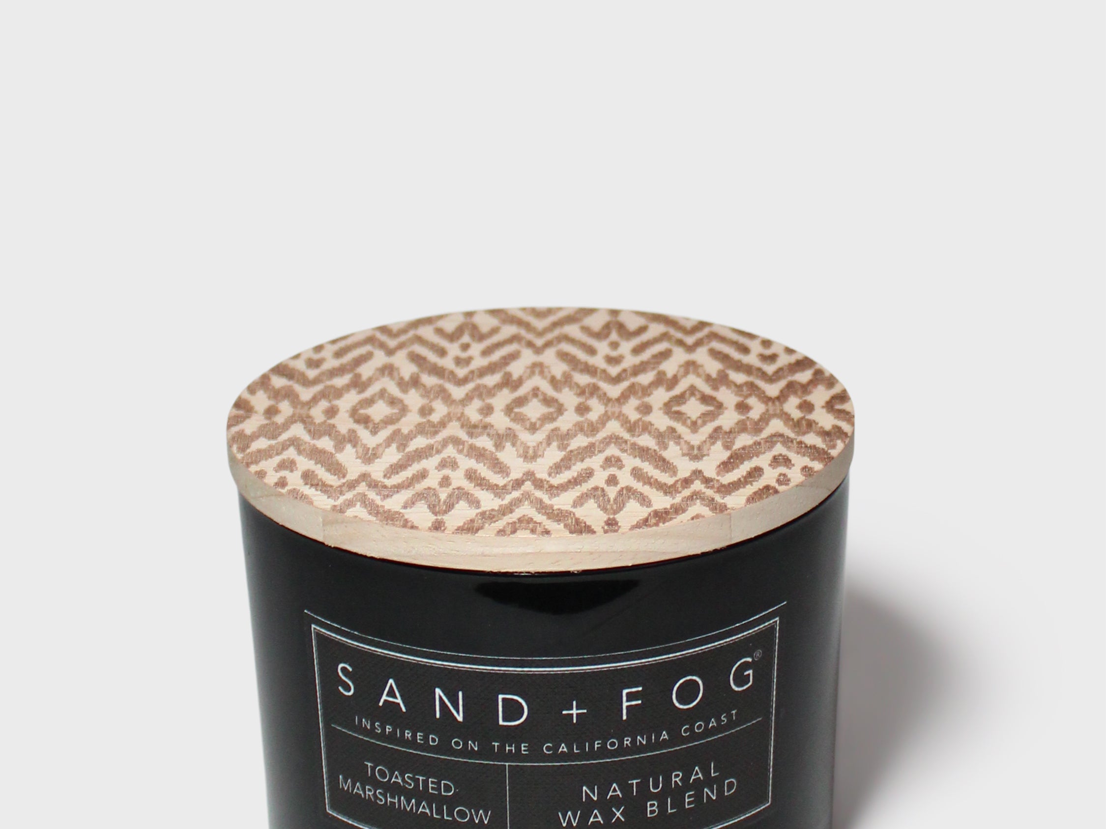 Black jar scented candle with beige patterned lid and Sand+Fog label