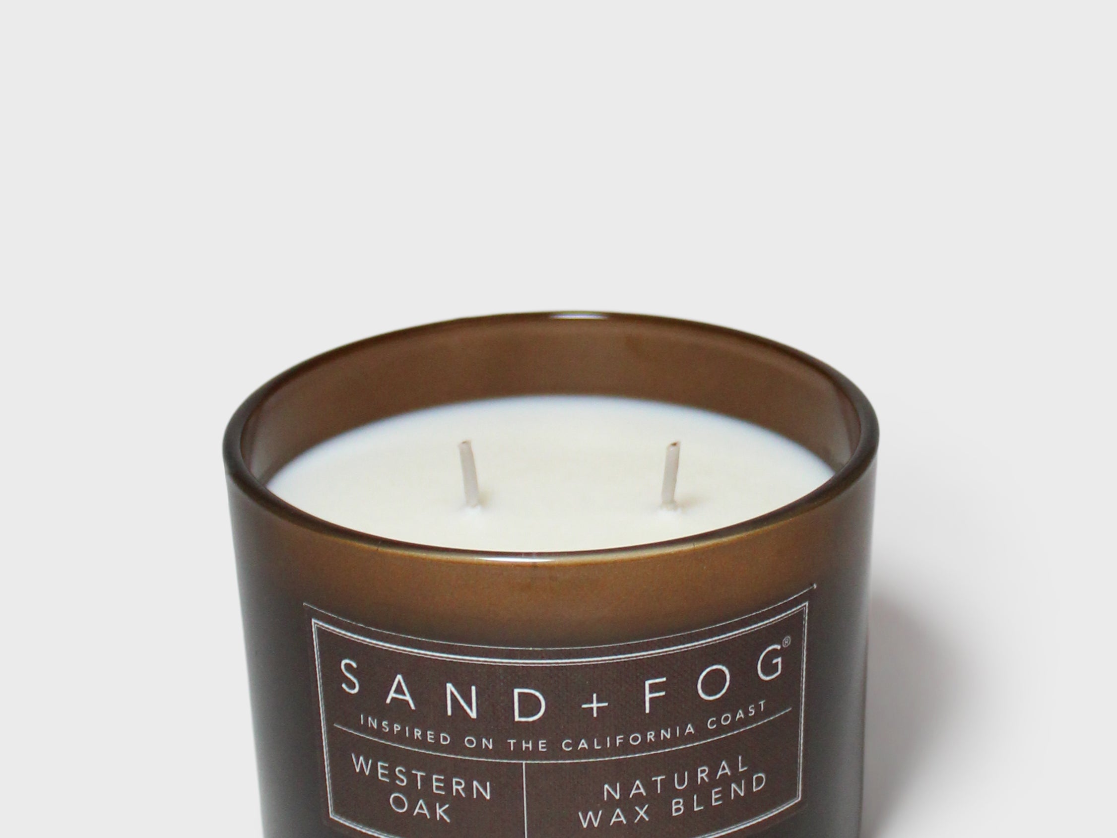 Scented candle in dark brown glass jar with two wicks and Sand+Fog label