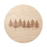 Round candle label with pine tree scene on light wood-grain background