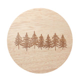 Round candle label with pine tree scene on light wood-grain background