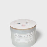 Crisp white scented candle with Sand + Paws label and cat face lid graphic