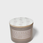 Sand+Fog candle jar in brown glass with vanilla label and white floral lid