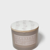 Sand+Fog candle jar in brown glass with vanilla label and white floral lid