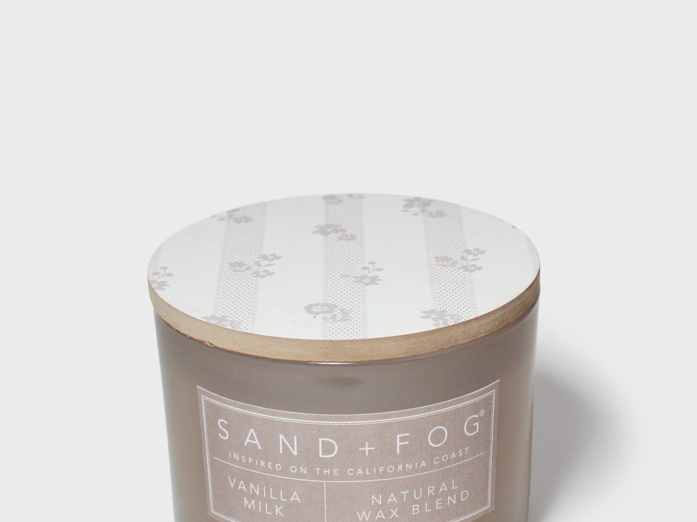 Sand+Fog candle jar in brown glass with vanilla label and white floral lid
