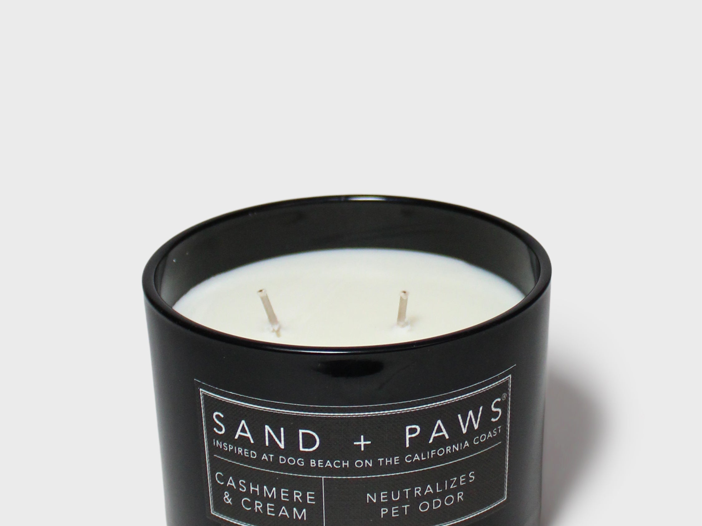 Black scented candle in glass jar, three wicks, Sand + Paws label and cream scent text