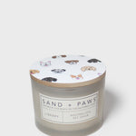Scented candle jar with 'Sand + Paws Library' label and paw print icons