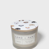 Scented candle jar with 'Sand + Paws Library' label and paw print icons