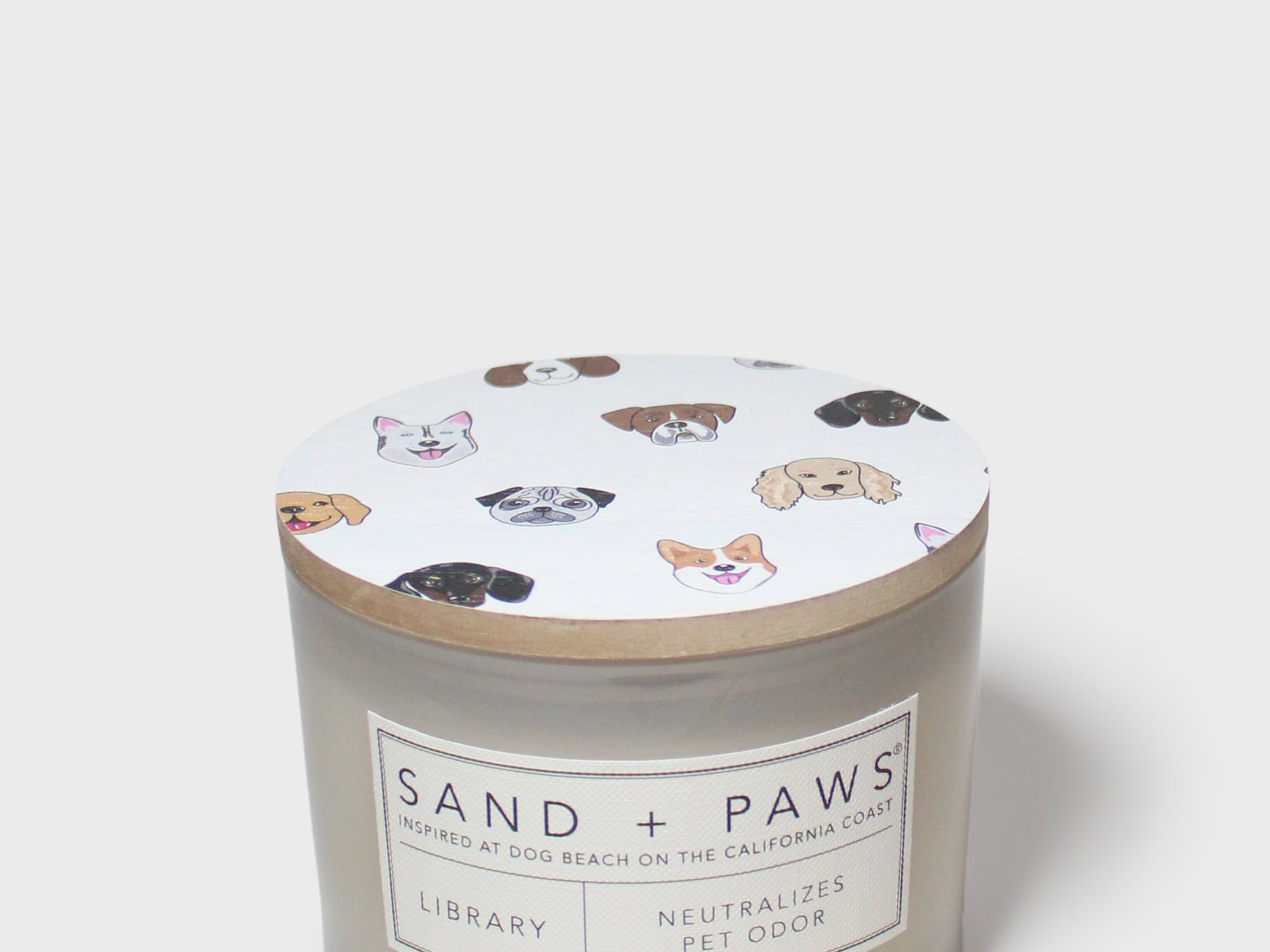 Scented candle jar with 'Sand + Paws Library' label and paw print icons