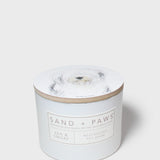Scented candle jar with dog portrait lid and 'Sand + Paws' label on front
