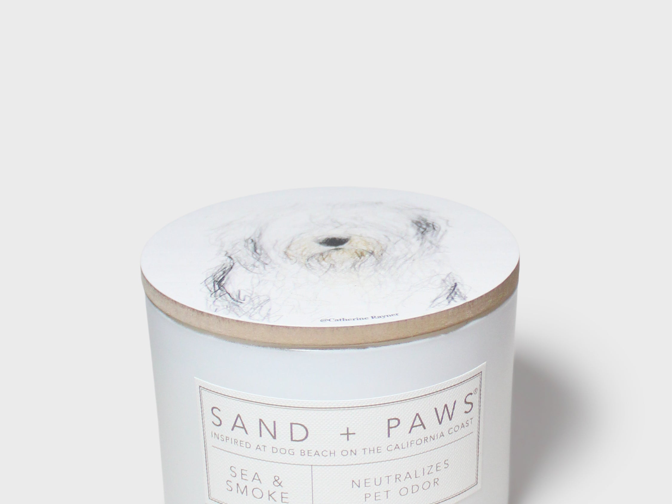 Scented candle jar with dog portrait lid and 'Sand + Paws' label on front