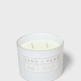 Scented candle jar with 'Sand + Paws' label, two wooden wicks visible