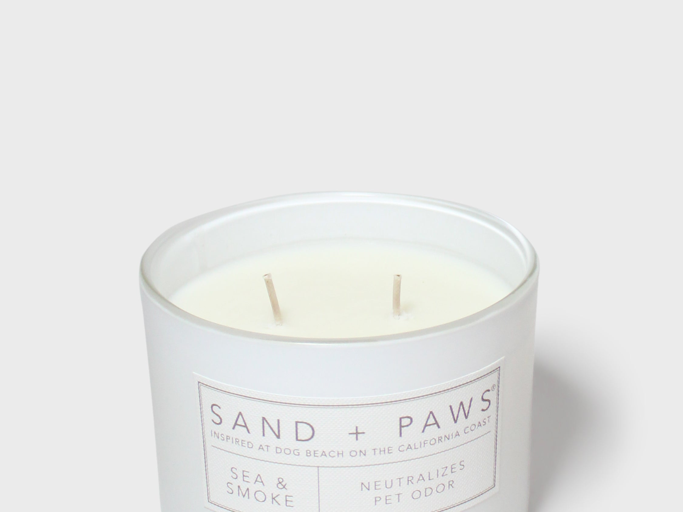 Scented candle jar with 'Sand + Paws' label, two wooden wicks visible