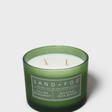 Green glass scented candle with white wax, two wicks, and SAND+FOG label