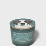 Scented candle in dark teal glass jar with "Sand + Paws" dog graphic lid