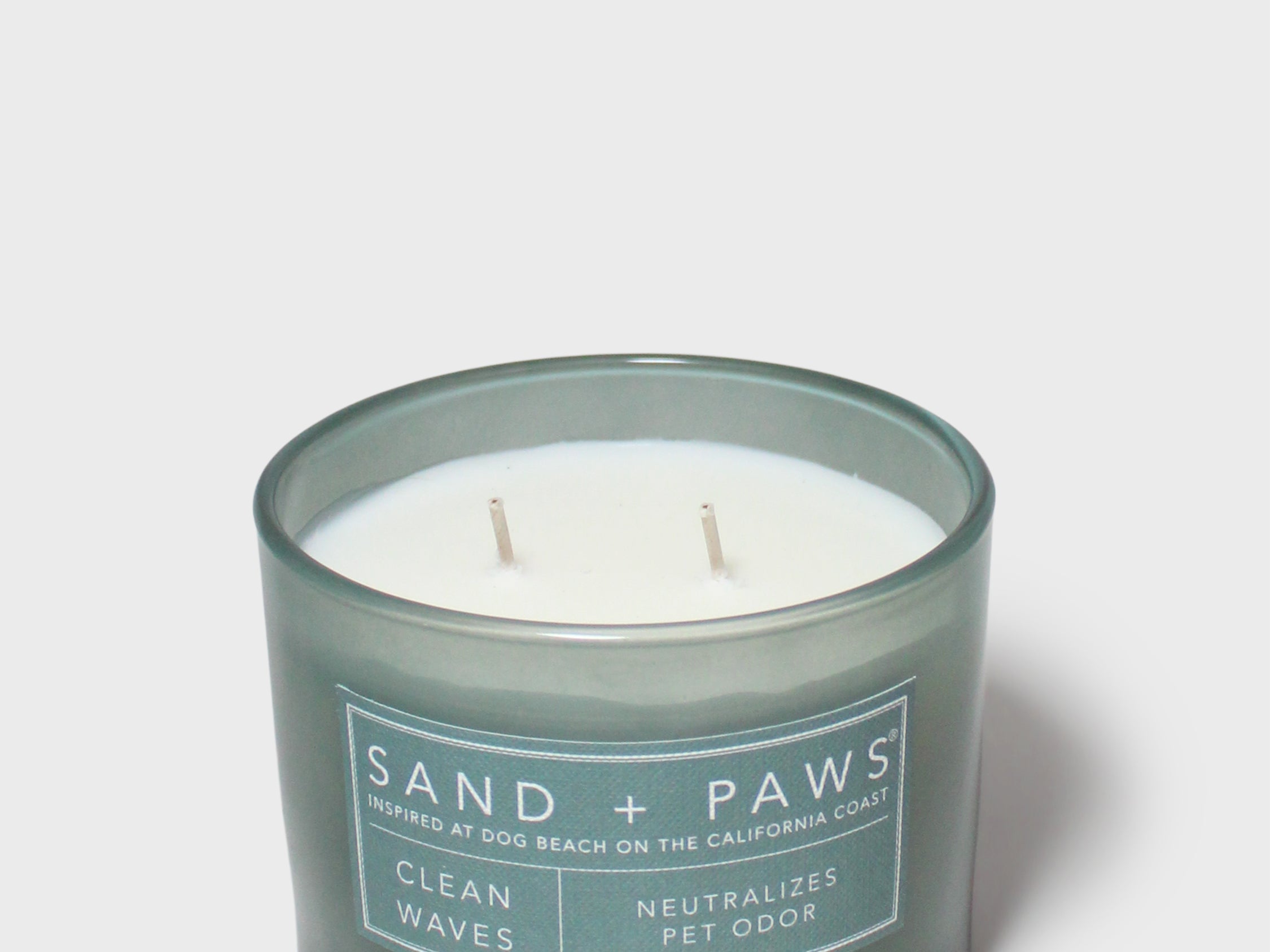 Scented candle in dark teal glass jar with "Sand + Paws" beach dog label