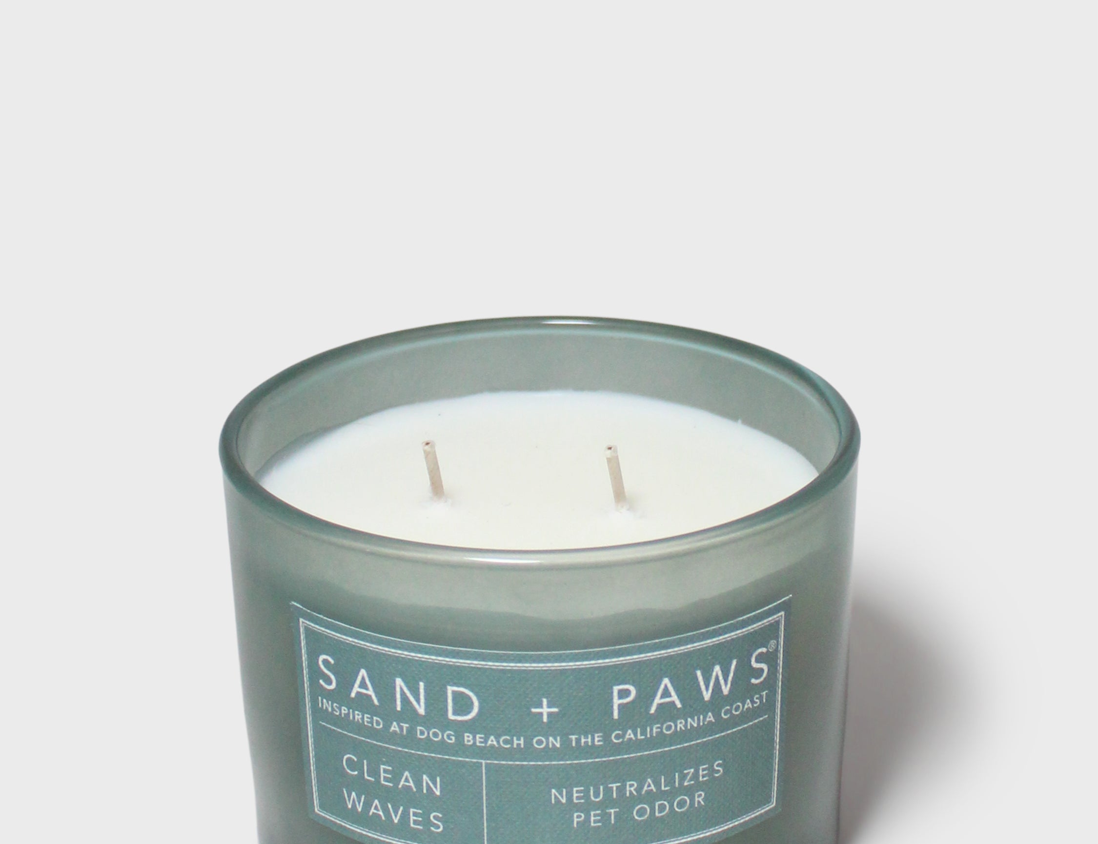 Scented candle in dark teal glass jar with "Sand + Paws" beach dog label