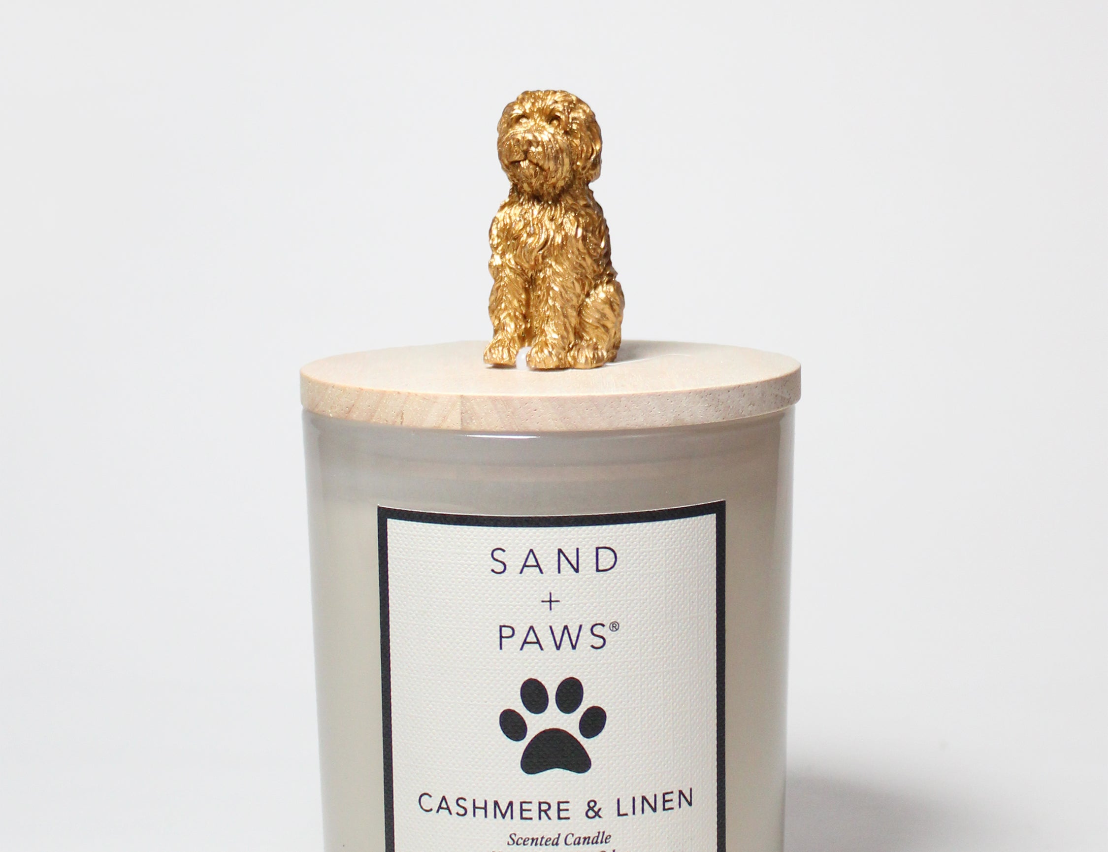 Scented candle in frosted glass jar with Sand + Paws Cashmere & Linen label, gold dog topper