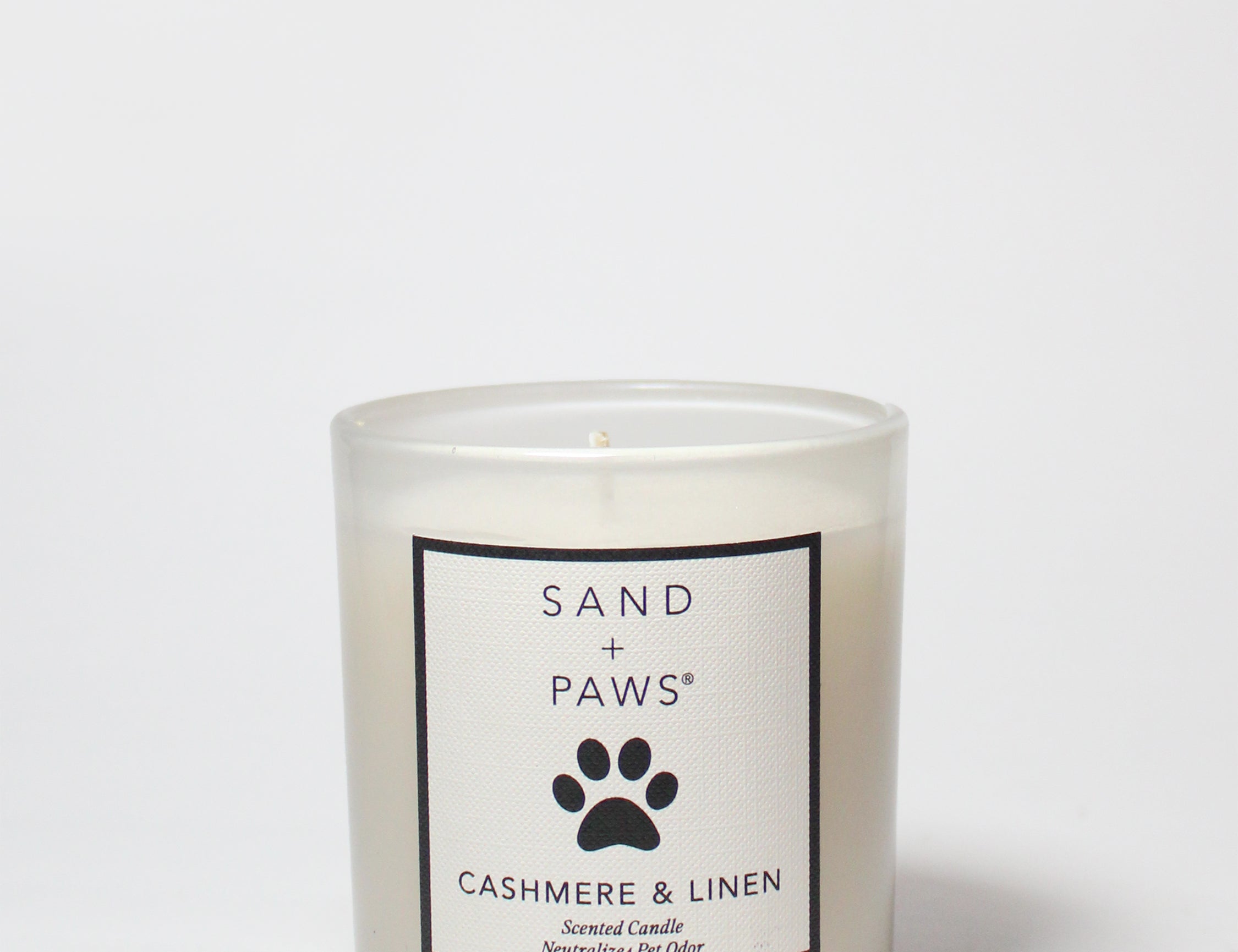 Scented candle in frosted glass jar with Sand + Paws Cashmere & Linen label, lit wick
