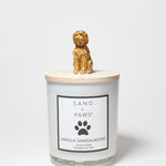 Scented candle jar with Sand + Paws Vanilla Sandalwood label and golden dog topper