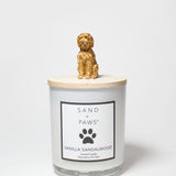 Scented candle jar with Sand + Paws Vanilla Sandalwood label and golden dog topper