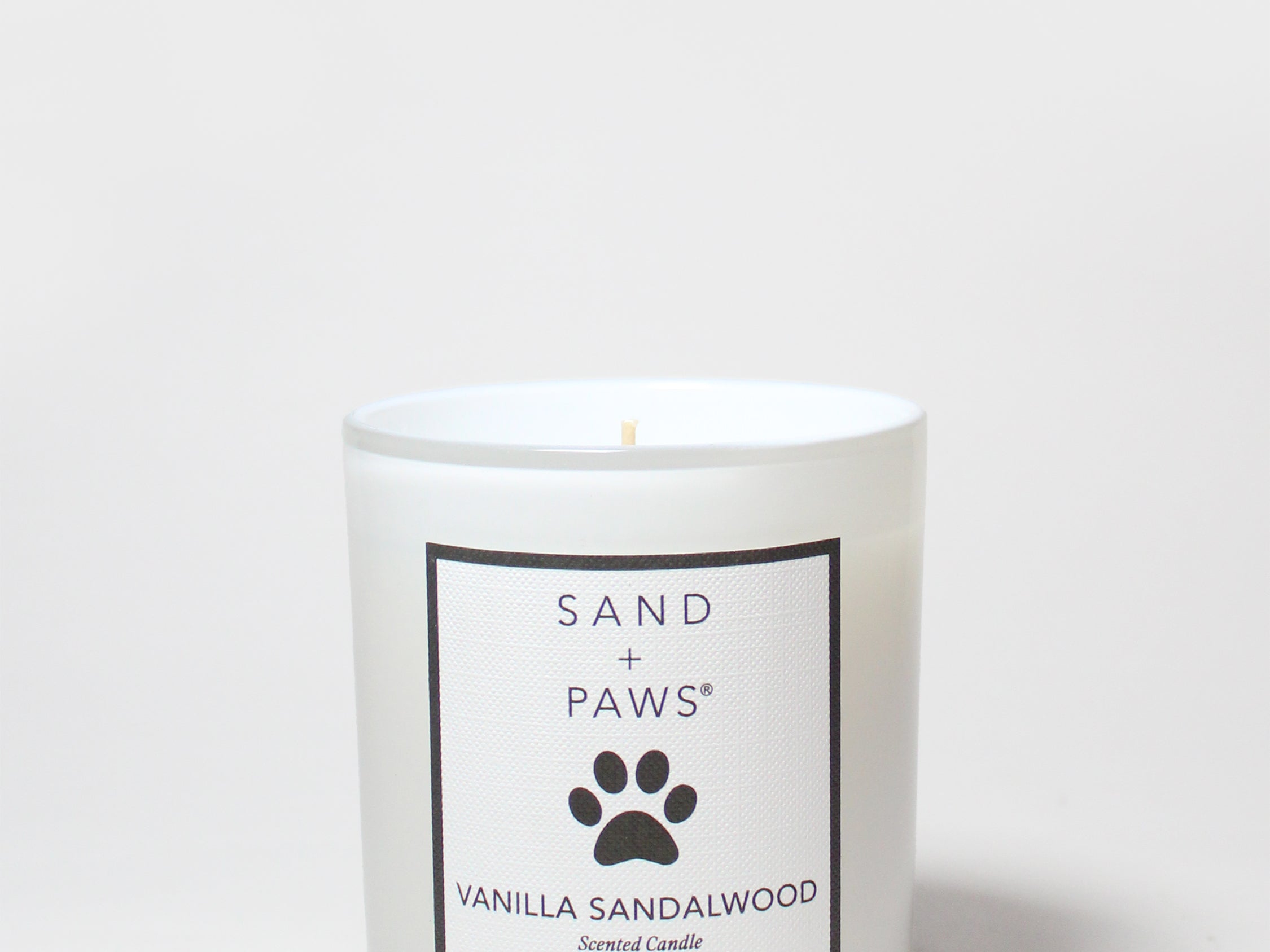 Scented candle in clear glass jar with Sand + Paws Vanilla Sandalwood label