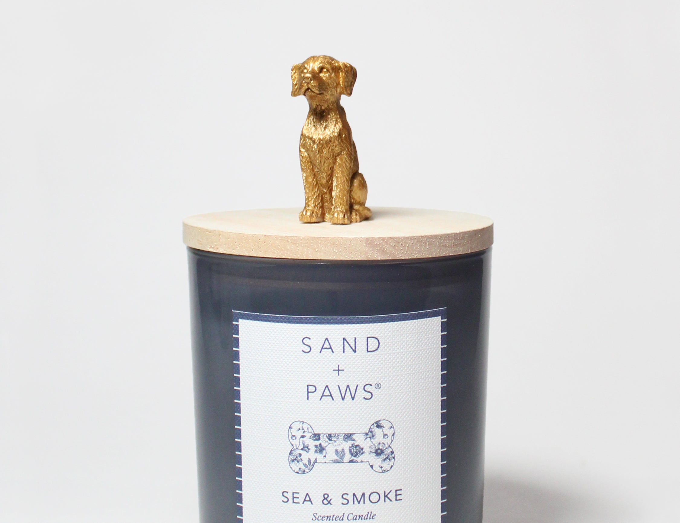 Sand + Paws scented candle in dark blue glass with Sea & Smoke label and gold dog topper