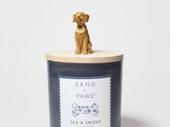 Sand + Paws scented candle in dark blue glass with Sea & Smoke label and gold dog topper