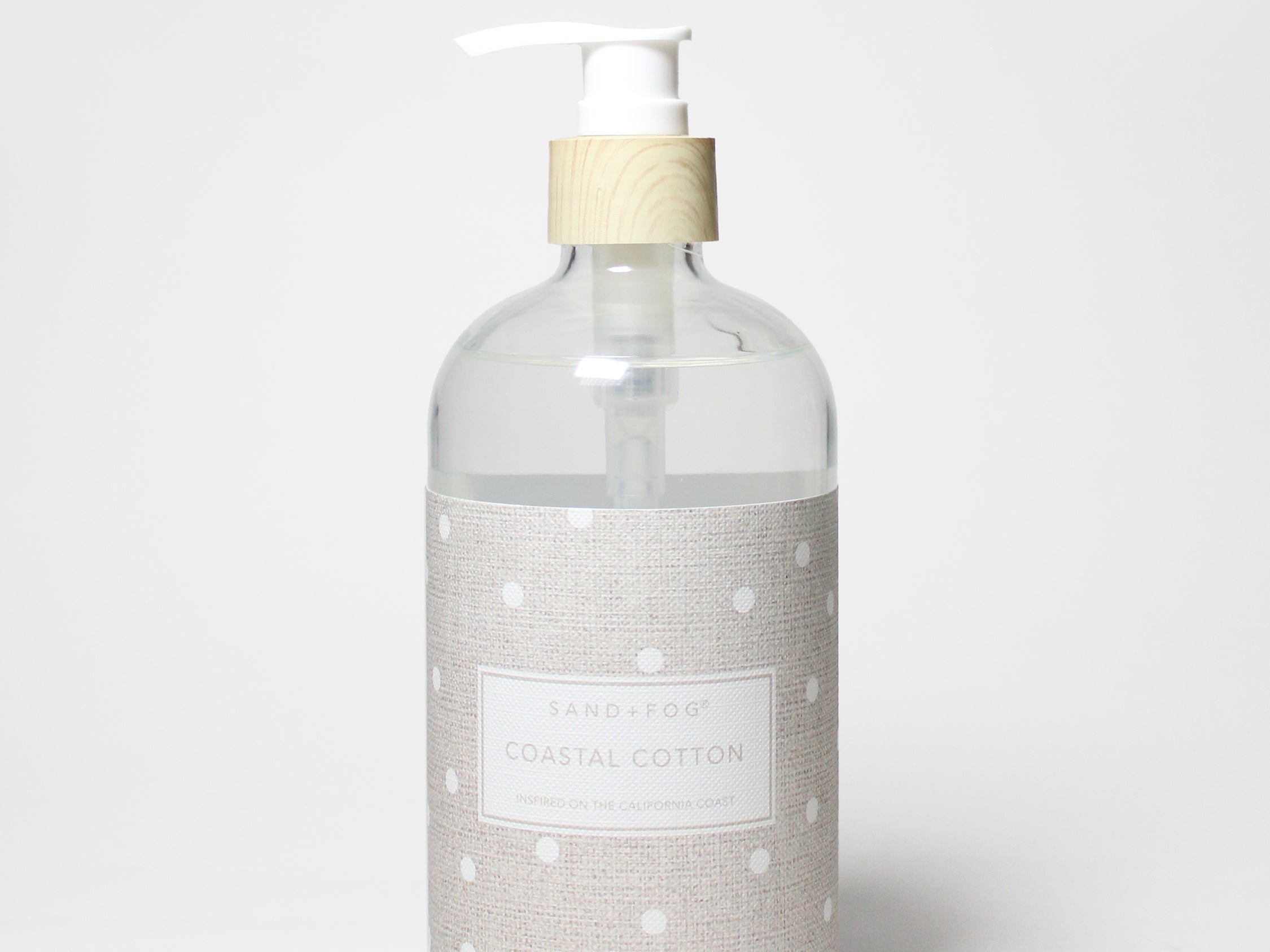 Liquid hand soap bottle with clear body, white pump, beige label with white dot pattern.