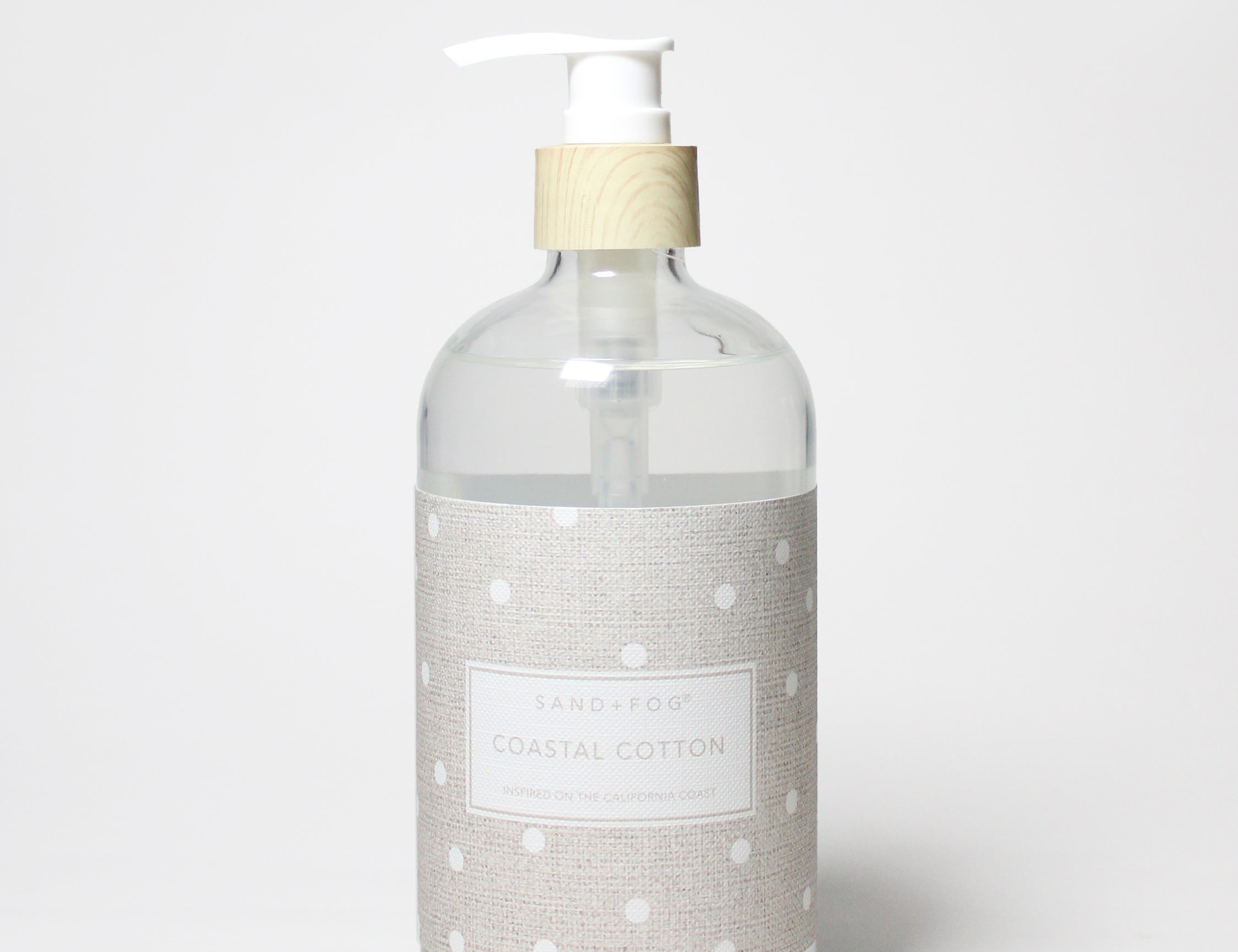 Liquid hand soap bottle with clear body, white pump, beige label with white dot pattern.