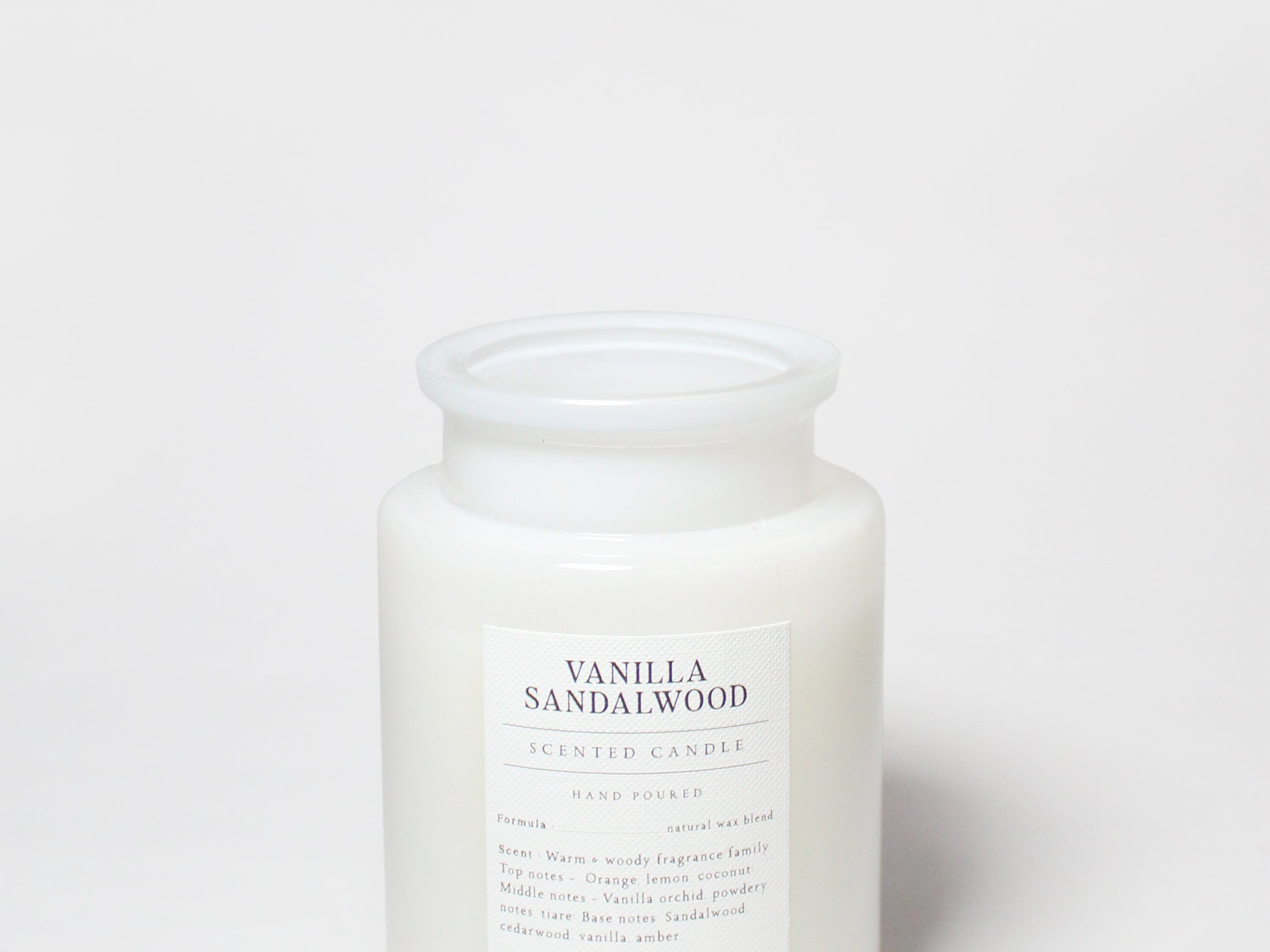 Scented candle in frosted white glass jar with printed label and white wax top