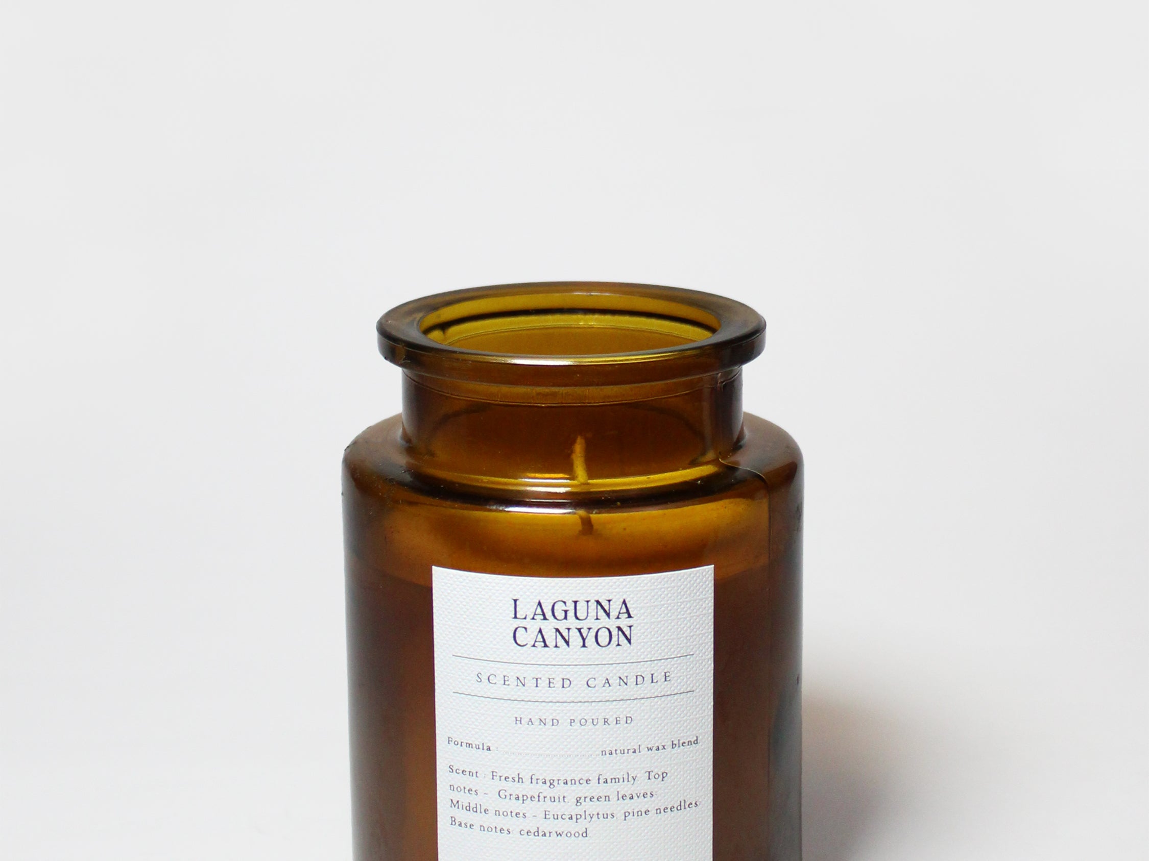 Amber glass scented candle jar with open top, visible wick, and Sand+Fog label