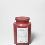 Maroon scented candle jar with Violet Sandalwood label; visible wax top.