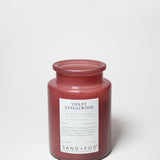 Maroon scented candle jar with Violet Sandalwood label; visible wax top.